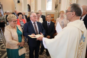 Zdjęcie przedstawia ludzi odbierających dyplomy od księdza we wnętrzu kościoła